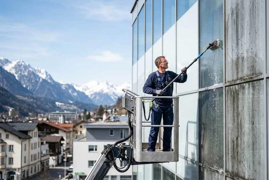 Fassadenreinigung in Tirol: Fachkraft reinigt eine Gebäudefassade, gereinigter und verschmutzter Bereich im Vergleich