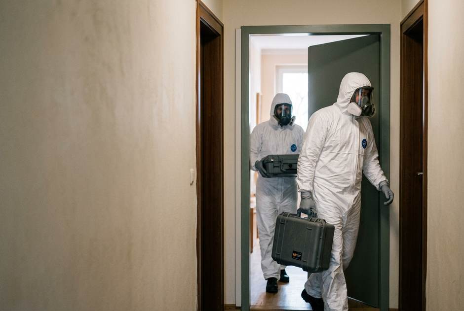Tatortreinigung in Tirol: Spezialisten in Schutzausrüstung mit Dekontaminationsausrüstung vor einer Wohnung